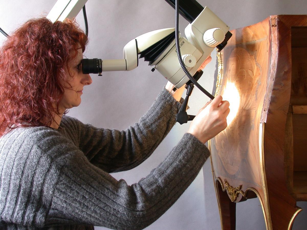 A restorer views a piece of furniture through a scope